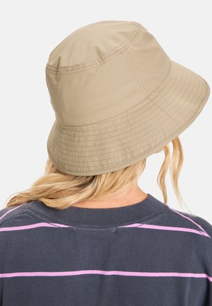 Beige bucket hat made of lightweight fabric, featuring a wide brim and stitched detailing. Worn with a dark shirt with pink stripes.