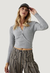 Top de manga larga con textura acanalada en gris con un diseño cruzado y detalles de botones, combinado con pantalones de pierna ancha a rayas de cintura alta que tienen bolsillos frontales.