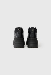 Melnas platformas kedas, kas aprīkotas ar gludu ādas augšdaļu, apaļu purngalu, polsterētu apkakli un drukātiem logo akcentiem uz papēža un sāniem.