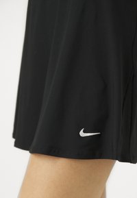 Mustast kerge kangaga spordiseelik, mille äärel on valge Nike logo ja õrnad vertikaalsed tekstuurid.