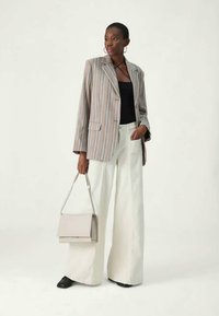 Striped blazer in muted colors, black top, wide white trousers, and light gray handbag. Smooth texture; oversized fit; minimal hardware accents.