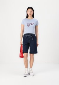 Camiseta corta azul claro con el logo "the gap", combinada con pantalones cortos de mezclilla oscuros y zapatillas altas blancas. Acento con un bolso de hombro rojo.
