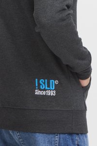 Sweat-shirt gris foncé avec des poignets et un ourlet côtelés, présentant un texte brodé bleu "! SLD Depuis 1993" sur le bas à gauche.