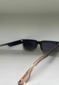 Zwarte en bruine gradient zonnebril met vierkante lenzen, metalen accenten en gemusterde pootjes, voorzien van donker getinte lenzen voor UV-bescherming.