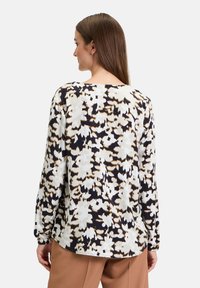 Langärmliges Oberteil mit floralem Muster in Schwarz, Creme und Braun. Weicher Stoff mit Rundhalsausschnitt und lockerer Passform, mit einem leicht abgerundeten Saum.