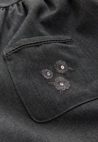 Poche en tissu gris foncé avec bordure cousue et trois petites fleurs brodées, chacune avec un centre en perle brillante.
