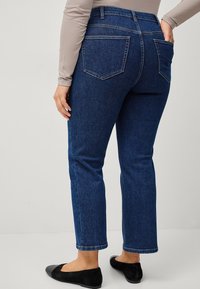 Donkerblauwe denim jeans met een recht model, voorzien van twee achterzakken en een tailleband. Gedragen met zwarte platte schoenen.