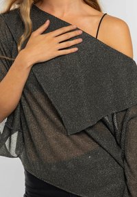 Top oscuro de textura metálica con un diseño asimétrico. La tela tiene un brillo sutil, presenta un corte holgado y el hombro visible.