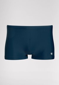 Námořnické modré plavkové šortky vyrobené z elastického materiálu, s hladkým povrchem, krátkými nohavicemi a malou cedulkou na levé straně.