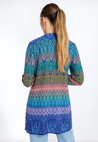 Knit cardigan with geometric pattern in blue, green, pink, and purple hues. Long sleeves, asymmetrical hem, and textured fabric.