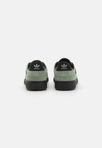 Gröna mockasneakers med svarta accenter, med en texturerad svart gummisula och embosserad logotyp på hälen och tungan.
