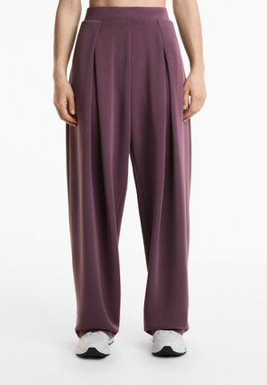 Loose-fitting, high-waisted trousers in a deep mauve fabric with pleats and a smooth texture, paired with white athletic shoes.