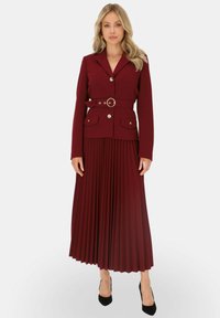Burgundowa, długi rękaw marynarka z dopasowanym talią i paskiem, w zestawieniu z plisowaną, midi spódnicą. Czarne szpilki dopełniają całość.