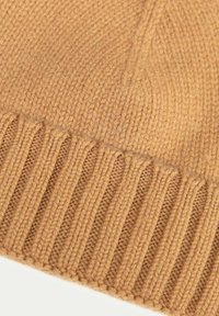 Bonnet en tricot beige avec une bande côtelée. Texture douce, design légèrement tombant, mettant en valeur des coutures fines et une couleur chaude.