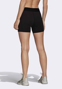 Shorts deportivos negros con una cinturilla ancha, que presentan un ajuste ceñido, una textura suave y detalles cosidos. Combinados con zapatillas gris claro.