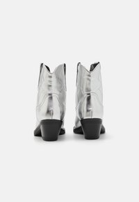 Botas de tobillo metálicas plateadas con un bajo tacón cuadrado, punta afilada, detalles de costura y un diseño inspirado en el estilo western.