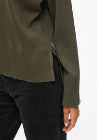 Maglione a coste verde olivo con orlo e polsini a costina, aperture laterali, abbinato a jeans neri. Tessuto morbido e vestibilità rilassata.