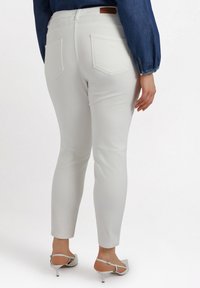 Jeans skinnys blancos con bolsillos traseros, cinturilla cosida y una textura suave, combinados con tacones plateados de tiras.