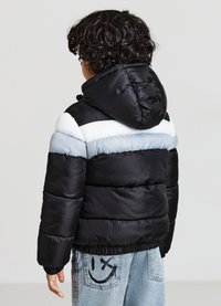 Veste matelassée avec un design en blocs de couleur noir, bleu et blanc. Elle comporte une capuche et des poignets côtelés, avec une texture lisse et brillante.