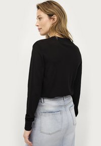 Black knit sweater with long sleeves and a round neckline, paired with light blue jeans featuring back pockets and a frayed hem.