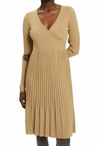 Brun ribbad omlotklänning med långa ärmar, som har en V-ringning och plisserad kjol. Den mjuka texturen och den åtsittande livstycket framhäver formen.