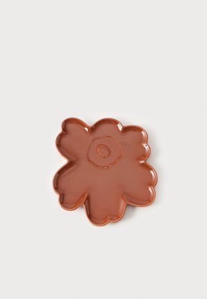 Glanzend bruin keramisch gerecht in de vorm van een bloem met afgeronde bloemblaadjes en een cirkelvormig detail in het midden op een effen lichte achtergrond.