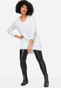 Witte tuniek met lange mouwen en een ronde halslijn, gecombineerd met glanzende zwarte leggings en gestudde zwarte enkellaarsjes. Gladde textuur overal.