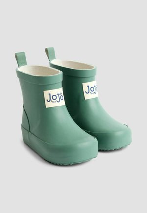 Vihreät kumisaappaat, joissa on vaalea sisustus, neliömäinen varvas, pieni korko ja takana vetonauhat; ominaisuutena logo, joka on kiinnitetty ulkopuolelle.