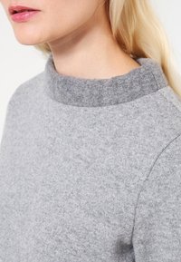 Szary, teksturowany sweter z dzianiny z wysokim, zaokrąglonym kołnierzem. Miękka tkanina, dopasowany krój i bezszwowe detale przy ramionach. Prosty i nowoczesny.