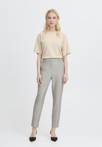 Béžový pletený krátký rukáv, šedé pouzdrové kalhoty a hnědé špičaté podpatky. Jednoduchý design, hladká textura, s neutrální barevnou paletou.