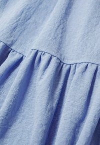 Tissu texturé bleu clair avec une couture froncée créant des plis doux et une apparence légèrement froissée.