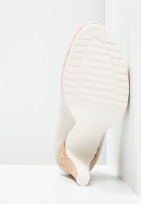 Beige high-heel shoe with a soft suede upper, a cork wedge heel, and a white rubber sole featuring horizontal grooves for traction.