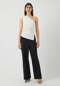 Top blanco asimétrico con una sola tira en el hombro, combinado con pantalones de pierna ancha negros y tacones a rayas en blanco y negro.