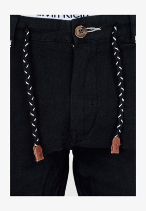 Pantalon noir avec une fermeture à bouton, doté d'un cordon de serrage avec des accents en cuir marron et un tissu texturé. Détail de couture visible.