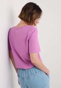 Tričko s krátkým rukávem a kulatým výstřihem v světle fialové barvě, doplněné elastickými kalhotami s vysokým pasem v světle modré barvě, které mají zadní kapsy.