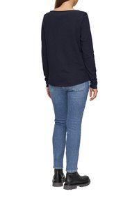 Lange mouwen marineblauw top, zachte stof, ronde halslijn, gecombineerd met lichtblauwe skinny jeans en zwarte enkellaarsjes met een dikke zool.