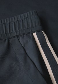 Svarta idrottsshorts med en strukturerad tyg, elastisk midja och kontrasterande beige ränder längs sidorna.