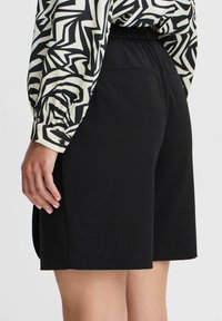 Zwarte shorts met een relaxte pasvorm, een elastische tailleband en twee achterzakken. Gecombineerd met een gestreepte blouse met lange mouwen in zwart-wit ontwerp.
