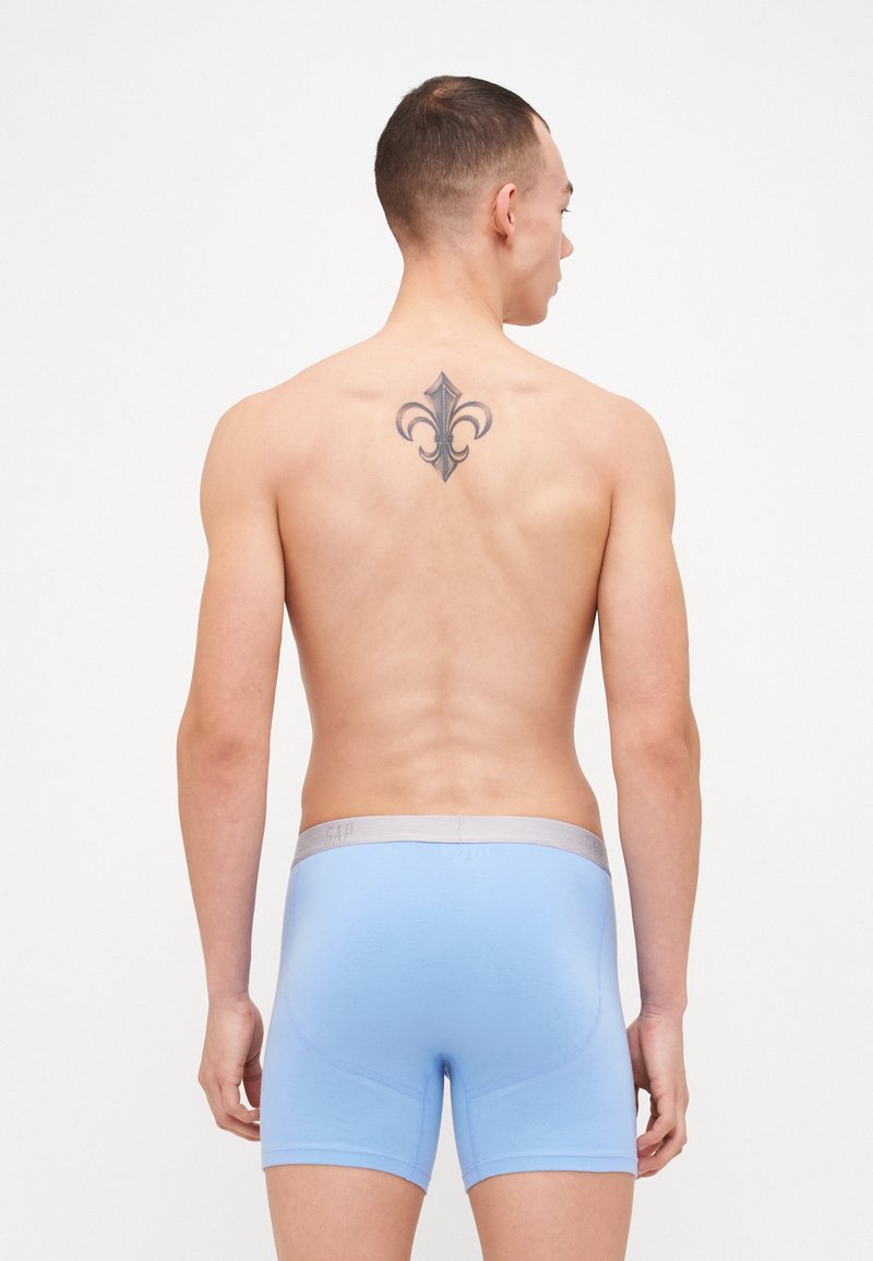 Boxers en coton bleu avec une taille en gris clair, présentant une texture lisse et un ajustement serré. Les détails notables incluent un logo sur la taille.