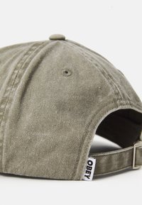 Olive green baseball cap viewed from the back with an adjustable strap and a white fabric tag labeled "OBEY."