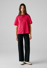 Rosa bomulls-t-shirt med korta ärmar och "RED BULL RACING" tryck. Kombinerad med svarta vida jeans och vita sneakers. Minimalistisk design.
