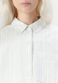 Camicia bianca con righe verticali blu e grigie, con colletto classico e taschino sul petto. Tessuto liscio e leggero.