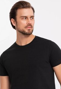 T-shirt nera a collo tondo realizzata in cotone. Maniche corte, design aderente, texture liscia. Aspetto semplice e minimalista senza pattern o accenti.