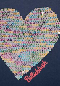 Fioletowe i pastelowe cekiny w kształcie serca na ciemnej tkaninie, z wyraźnym różowym logo "Billieblush".