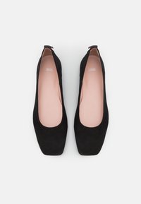 Ballerines en suède noir avec un bout arrondi, une doublure intérieure lisse et un petit accent rouge au talon. Semelle plate, design minimaliste, style polyvalent.