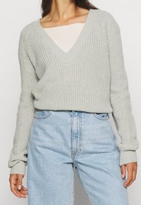 Jasnoszary sweter dziany z dekoltem w serek, ściągaczami na mankietach i luźnym krojem, w zestawieniu z jasnoniebieskimi spodniami o wysokim stanie.