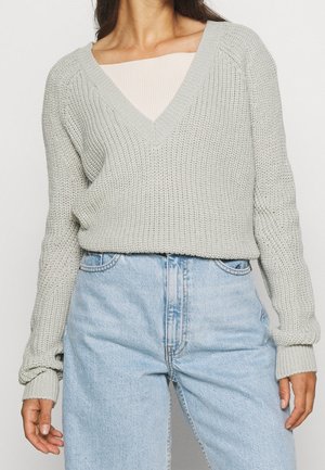 Lichtgrijze gebreide trui met een V-hals, geribbelde manchetten en een losse pasvorm, gecombineerd met lichtblauwe hoog getailleerde jeans.