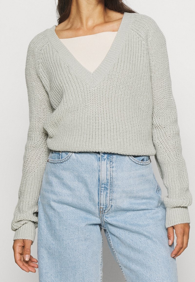 Jasnoszary sweter dziany z dekoltem w serek, ściągaczami na mankietach i luźnym krojem, w zestawieniu z jasnoniebieskimi spodniami o wysokim stanie.