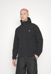 Μαύρο μπουφάν με φερμουάρ μπροστά, κουκούλα, πλαϊνές τσέπες και ελαστικούς καρπούς. Διαθέτει αντίθετο ραφές και ένα μικρό λογότυπο στο στήθος.