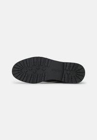 Suela de zapato de goma negra con patrón de relieve texturizado y nombre de la marca grabado. Cuenta con ranuras y áreas elevadas para mayor tracción.